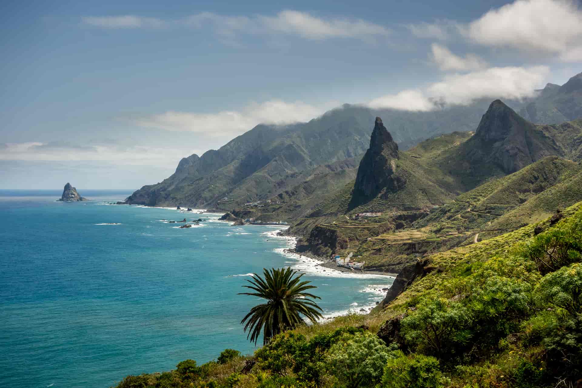 Rugged green mountains meet turquoise sea on the North coast of Tenerife, with a sea stack visible.