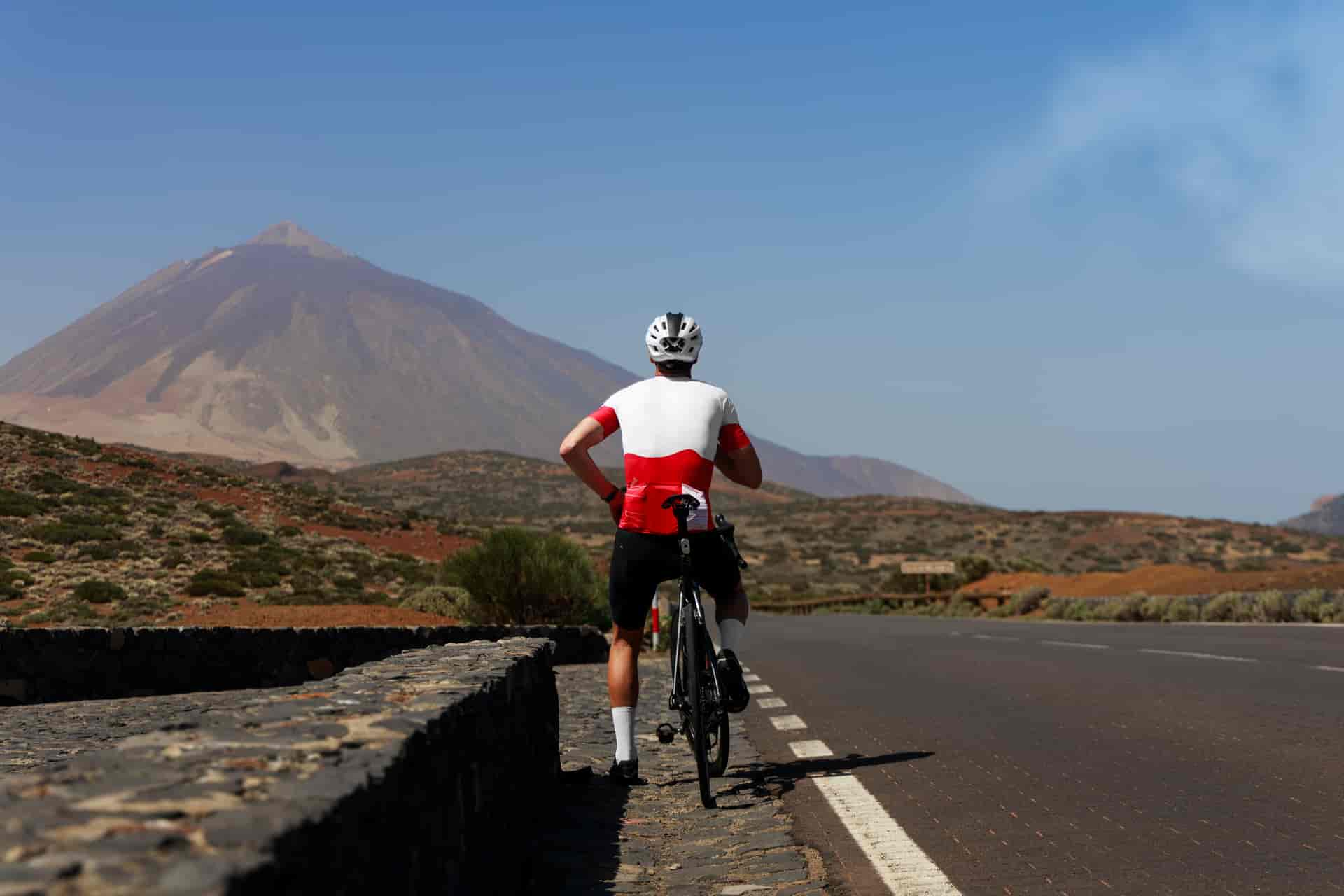 Cyclist with bicycle pauses by a road overlooking a large mountain in Tenerife.