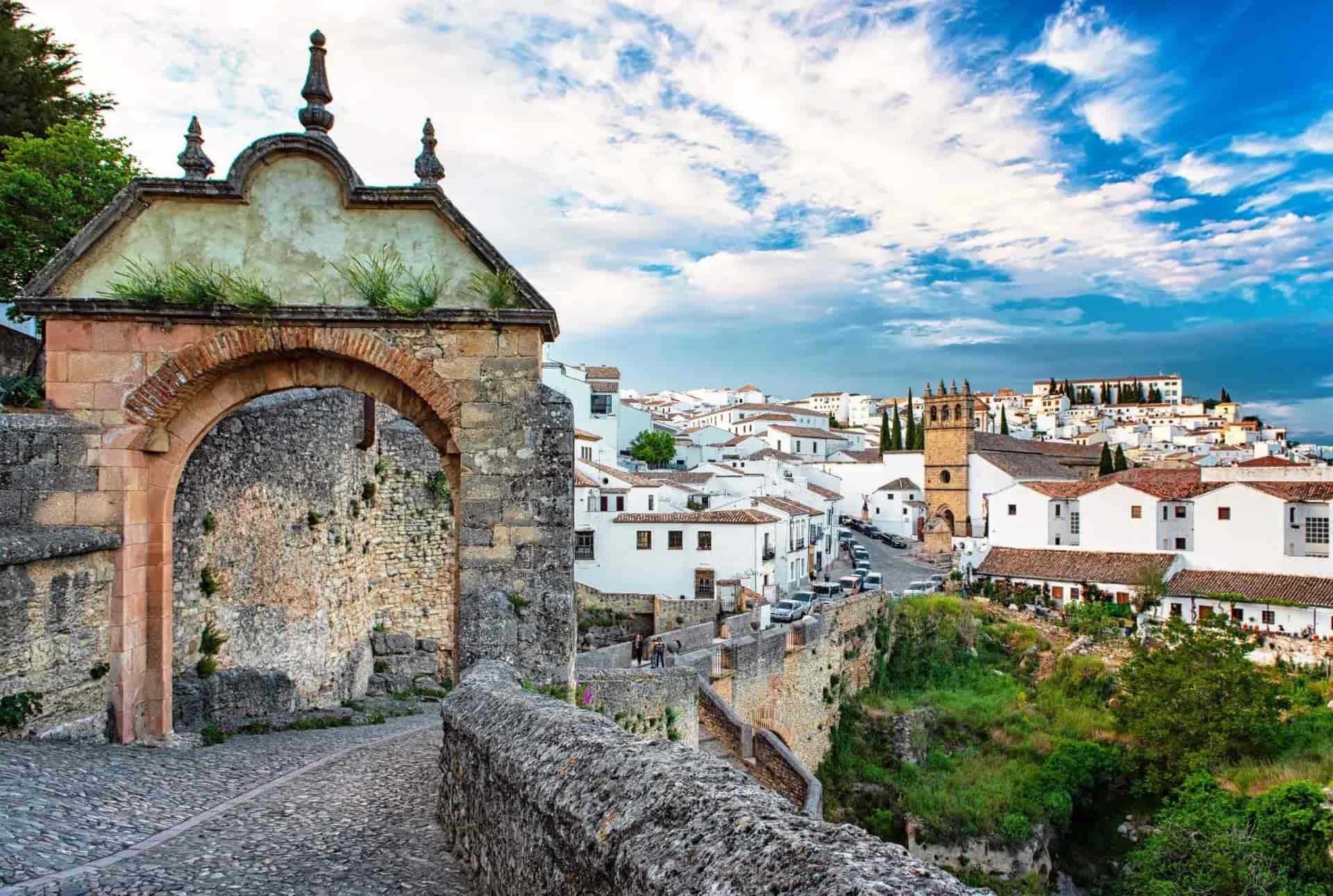 Stone archway entrance to the old town of Ronda, Spain with white buildings and church tower.