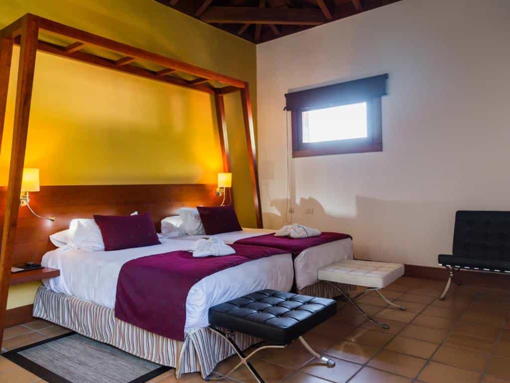 Twin beds with purple accents under a wooden canopy frame in a room with yellow walls.