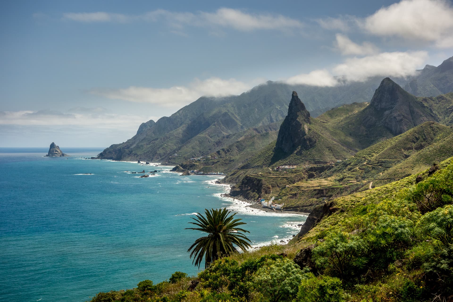 Rugged green mountains meet turquoise sea on the North coast of Tenerife, with a sea stack visible.