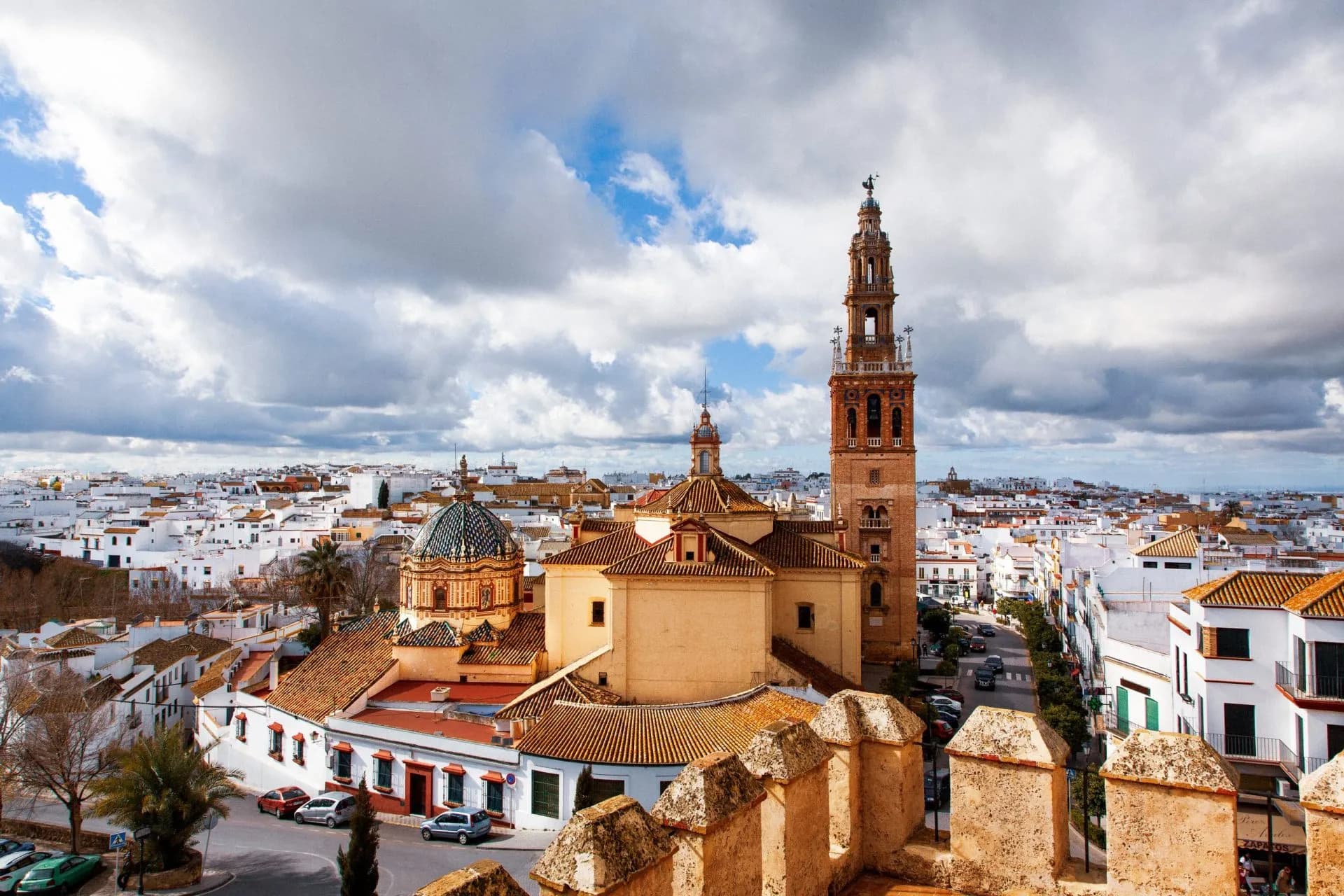 View of Carmona, Sevilla, featuring a church tower and white buildings under a cloudy sky.