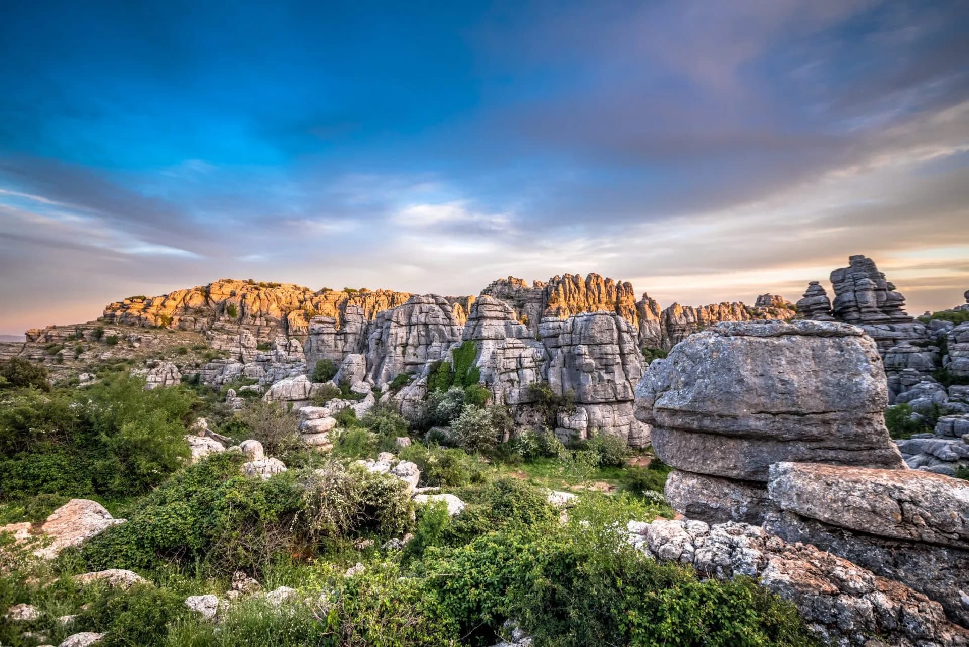 Karst rock formations and green scrubland at Torcal de Antequera under a dramatic sunset sky.