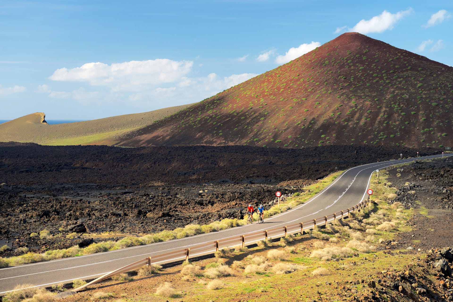Cyclists cross lava landscape on the LZ-704 road coming from El Golfo. Timanfaya National Park, Lanzarote, Canary Islands, Spain