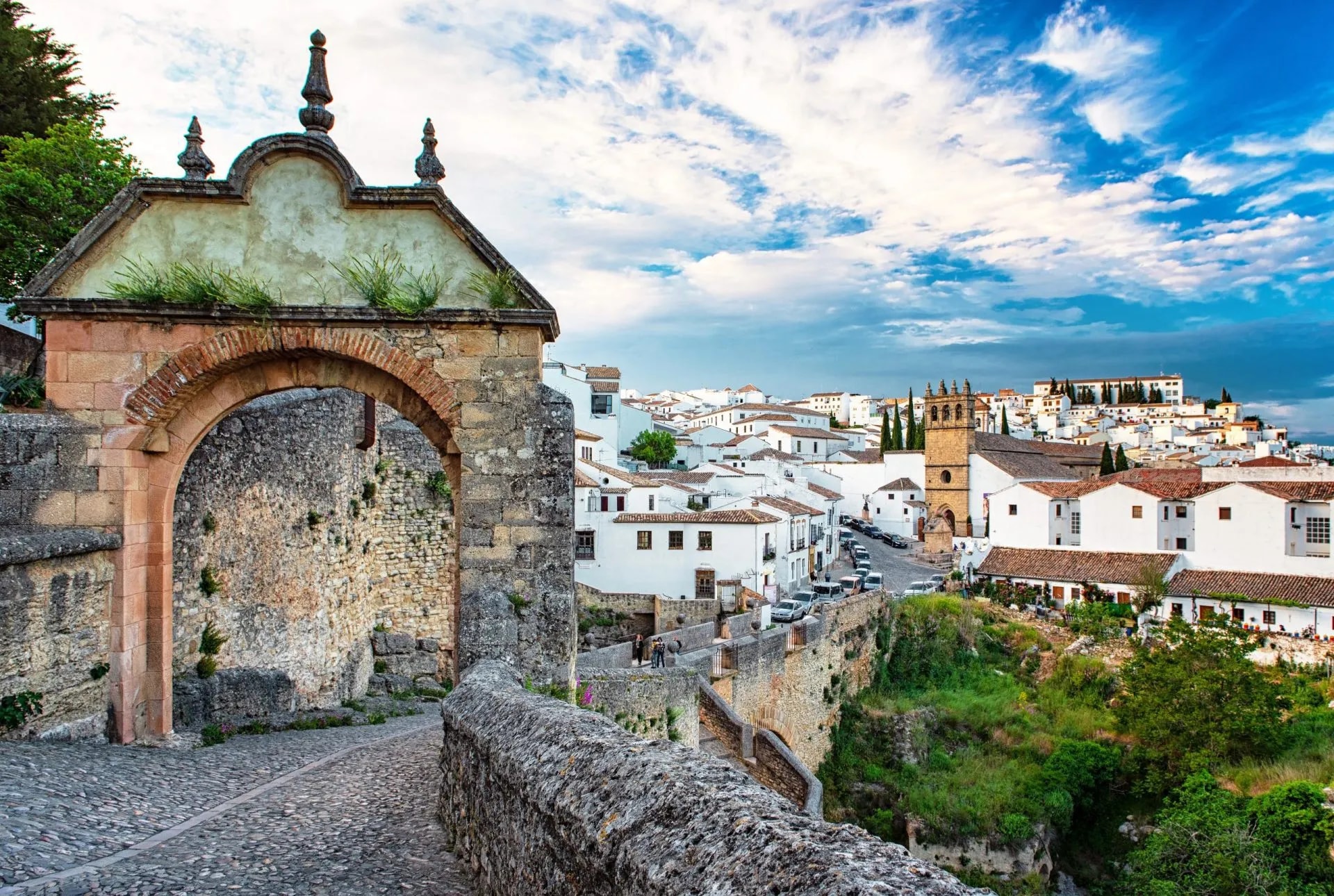 Stone archway entrance leading to white buildings of the old town of Ronda, Spain.