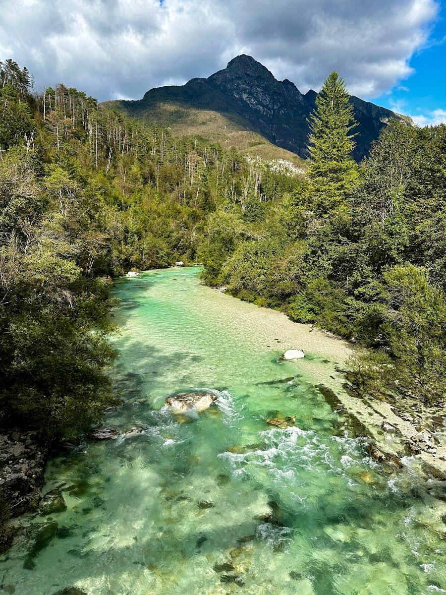 River with clear turquoise water flowing past forested slopes and a dark mountain peak.