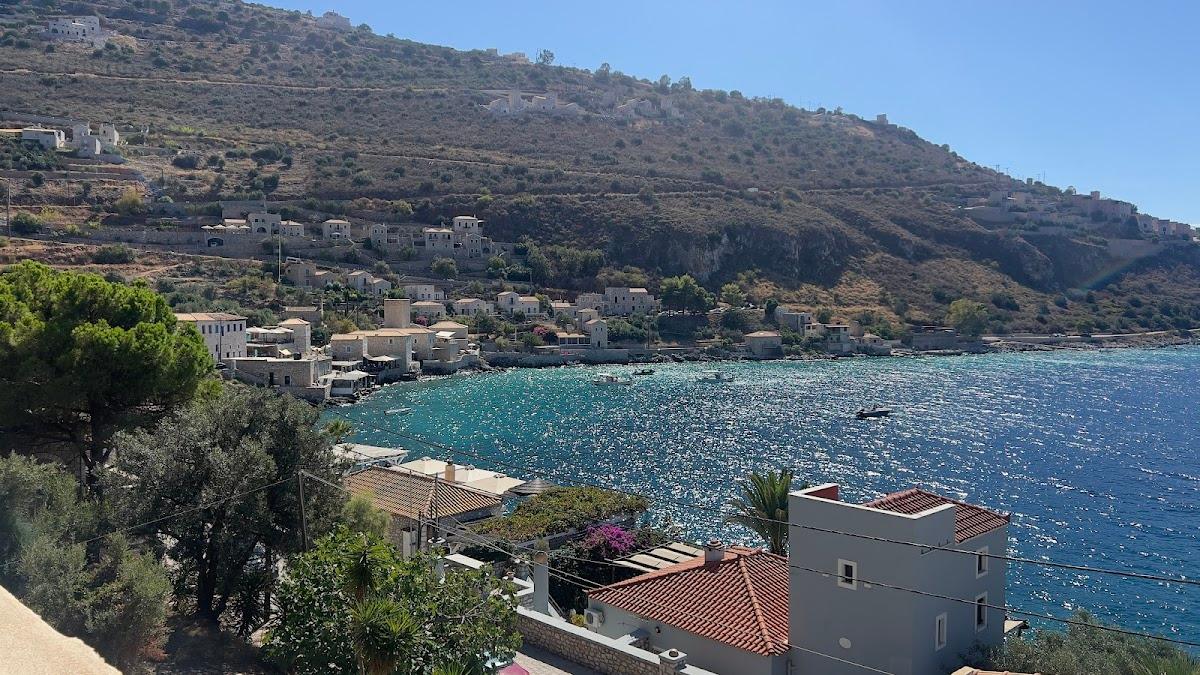 Coastal village with stone houses climbing a dry hillside above sparkling turquoise sea water.