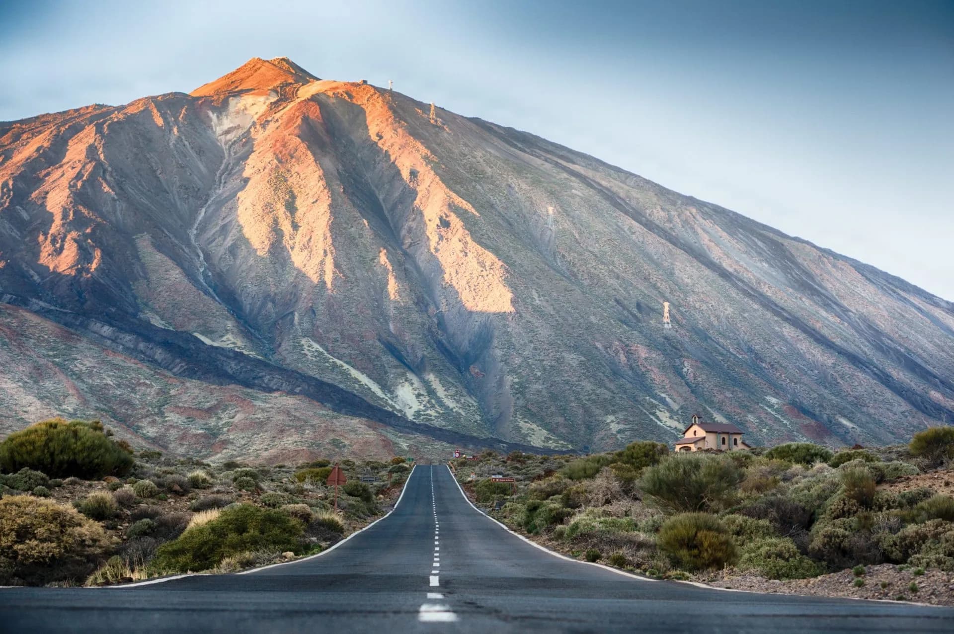 Road leading to large volcano peak, with small building in foreground landscape, El Teide.