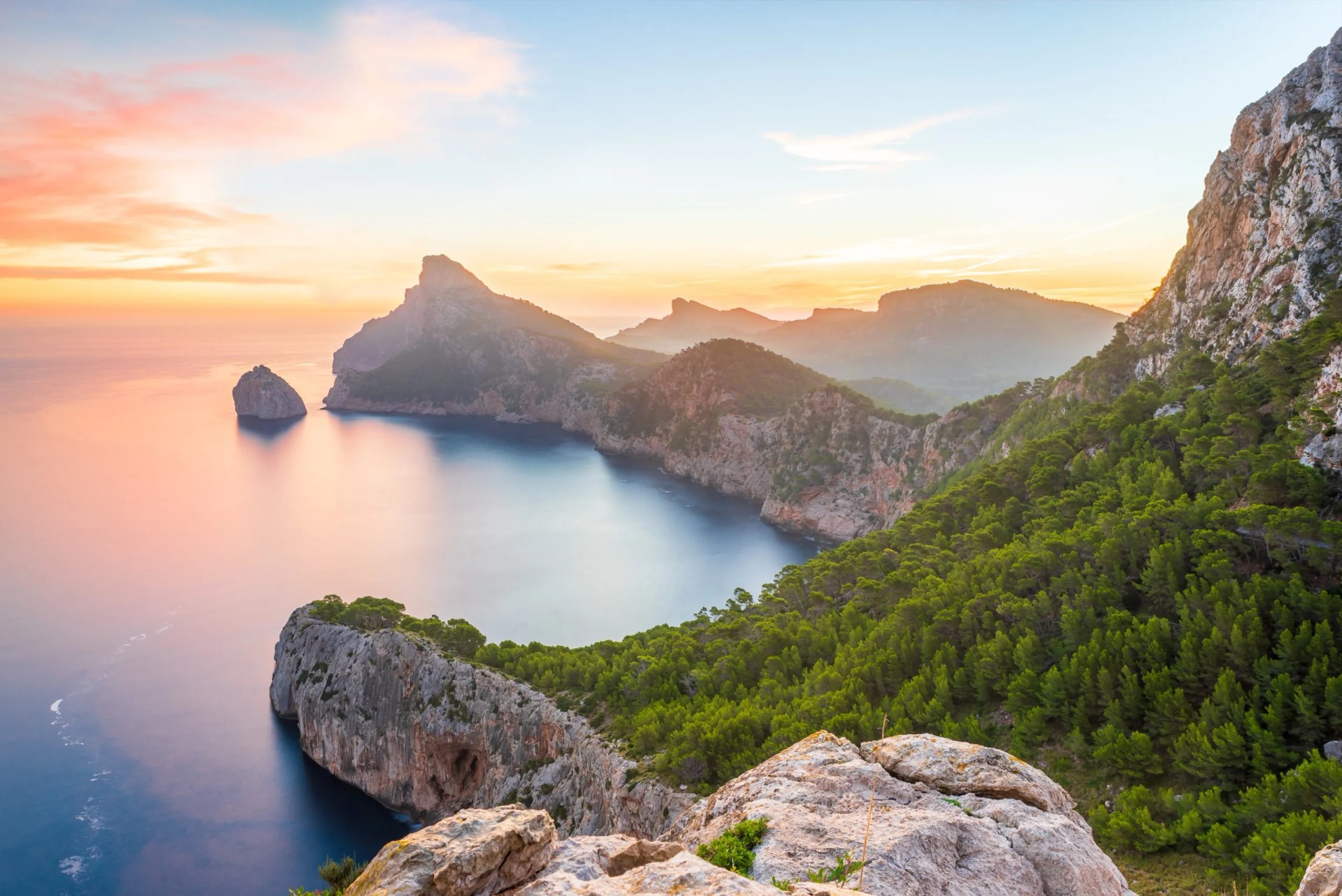 Panoramic view of Cap de Formentor cliffs and sea at sunrise with pink and blue sky.