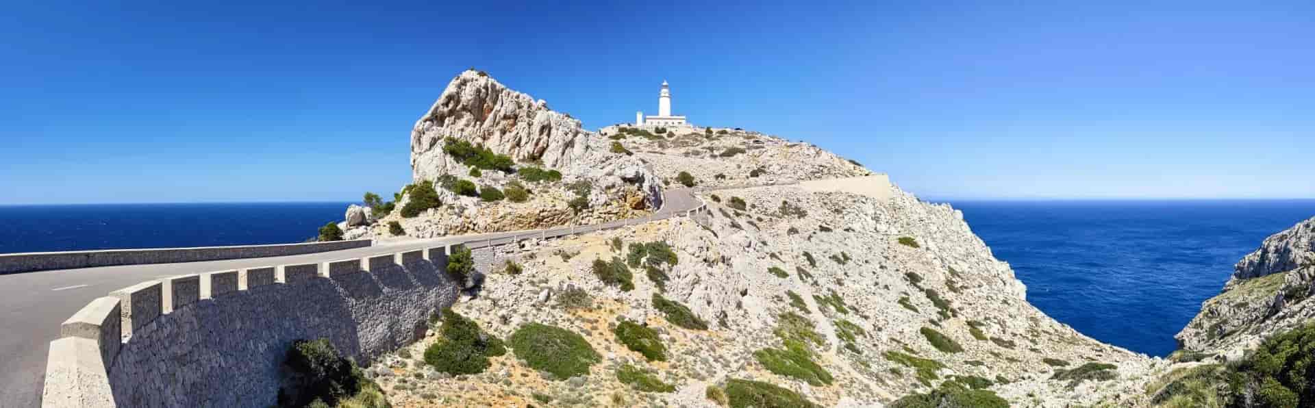 Lighthouse on rocky headland above winding road and deep blue Mediterranean Sea at Cap Formentor.