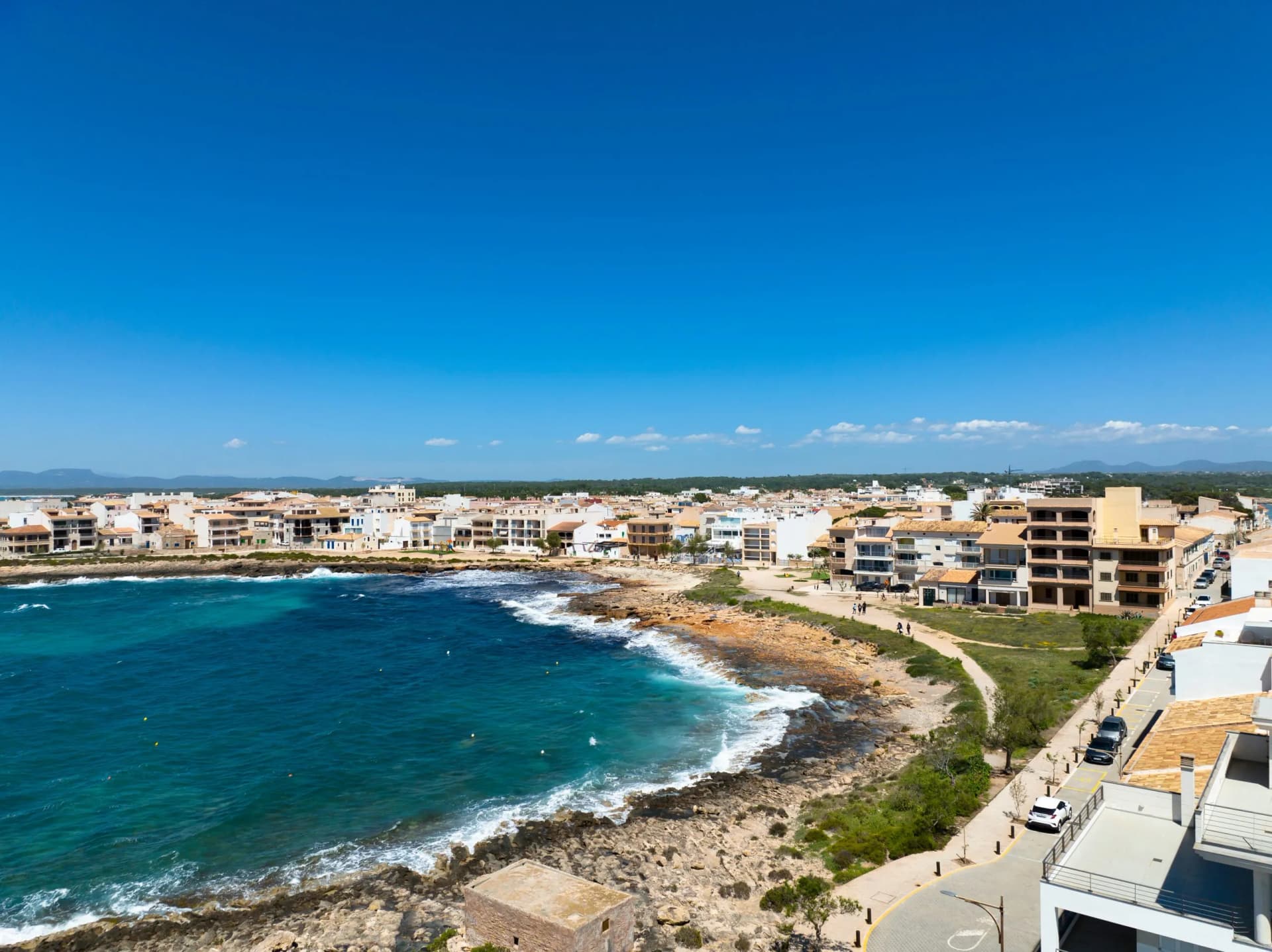 Aerial view of coastal town with white buildings, turquoise sea, and rocky shore in Colonia de Sant Jordi, Mallorca.