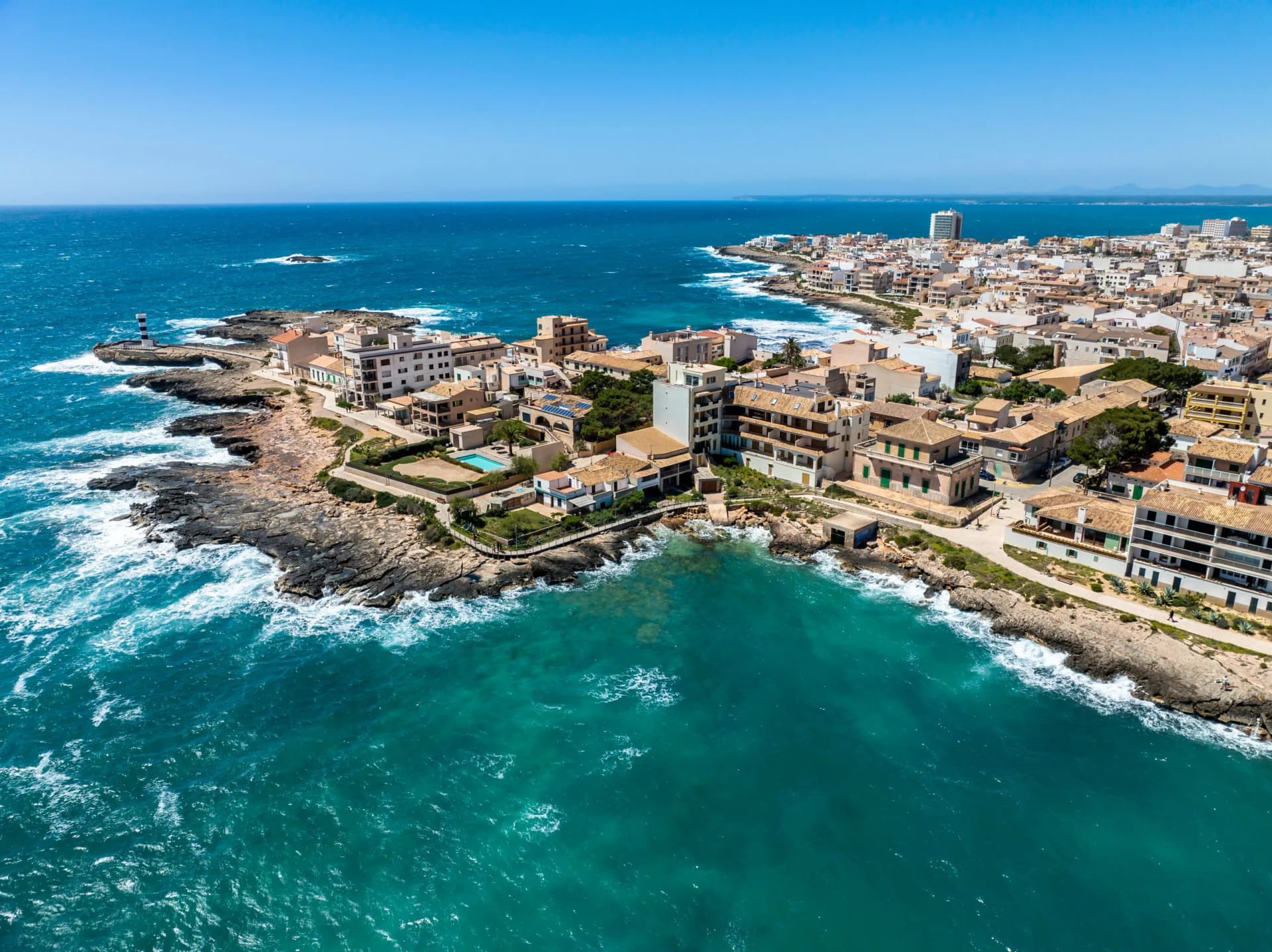 Aerial view of Colonia de Sant Jordi, Mallorca, with buildings along rocky coastline and turquoise Mediterranean Sea.
