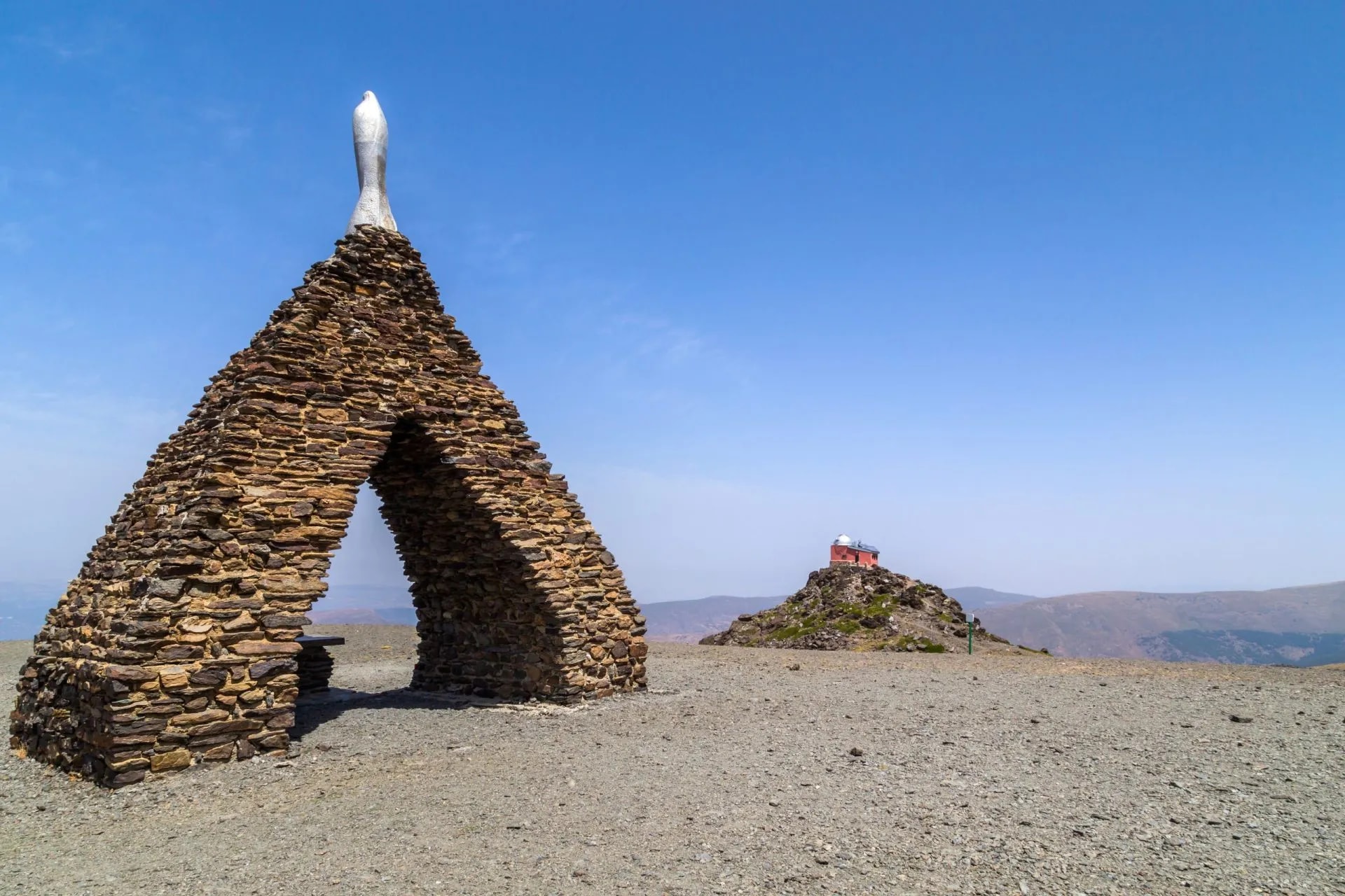 Monument to the Virgen de las Nieves with stone arch structure on a dry mountain landscape.