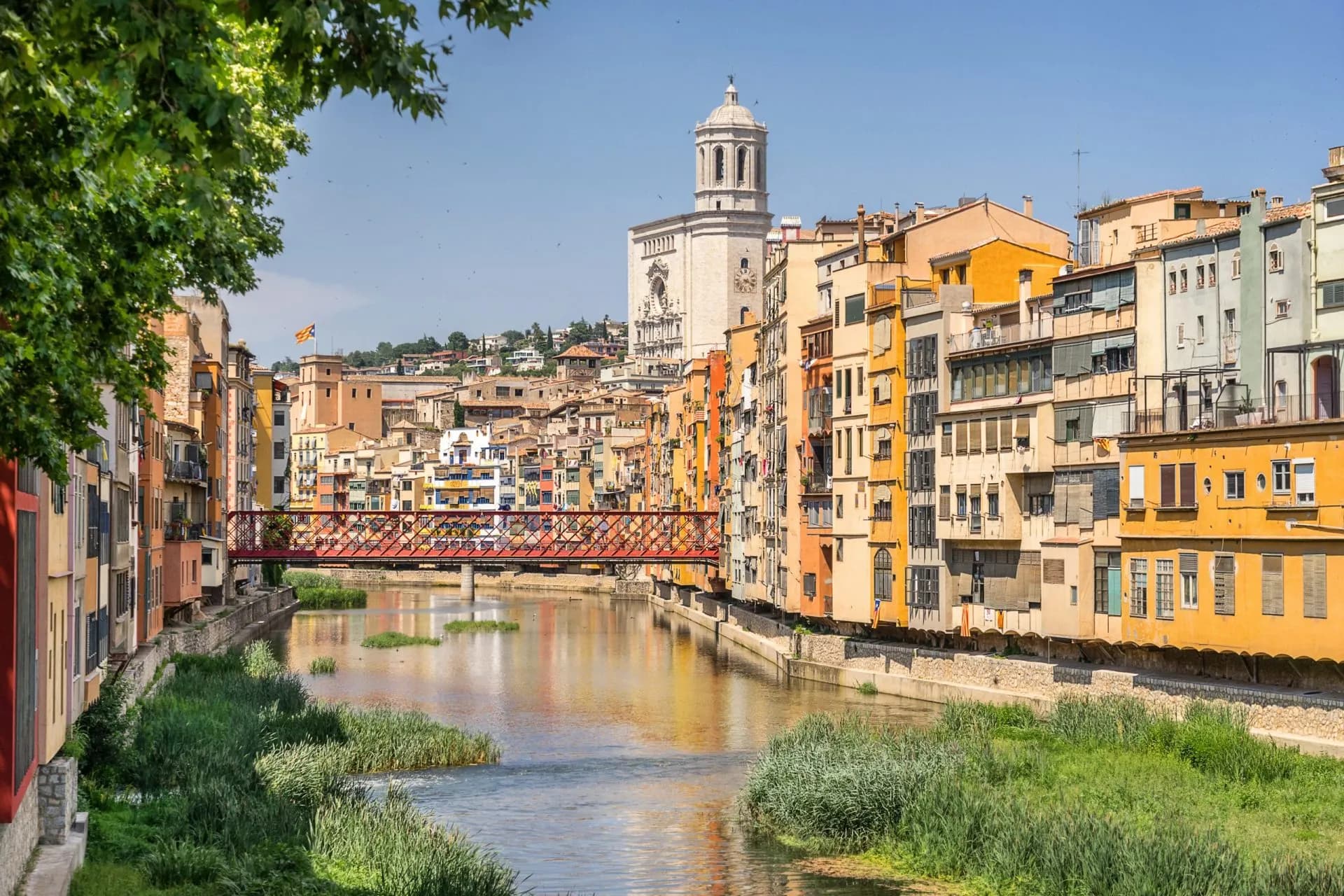 Colorful buildings line the Onyar River with a red bridge and Girona Cathedral in Catalonia, Spain.
