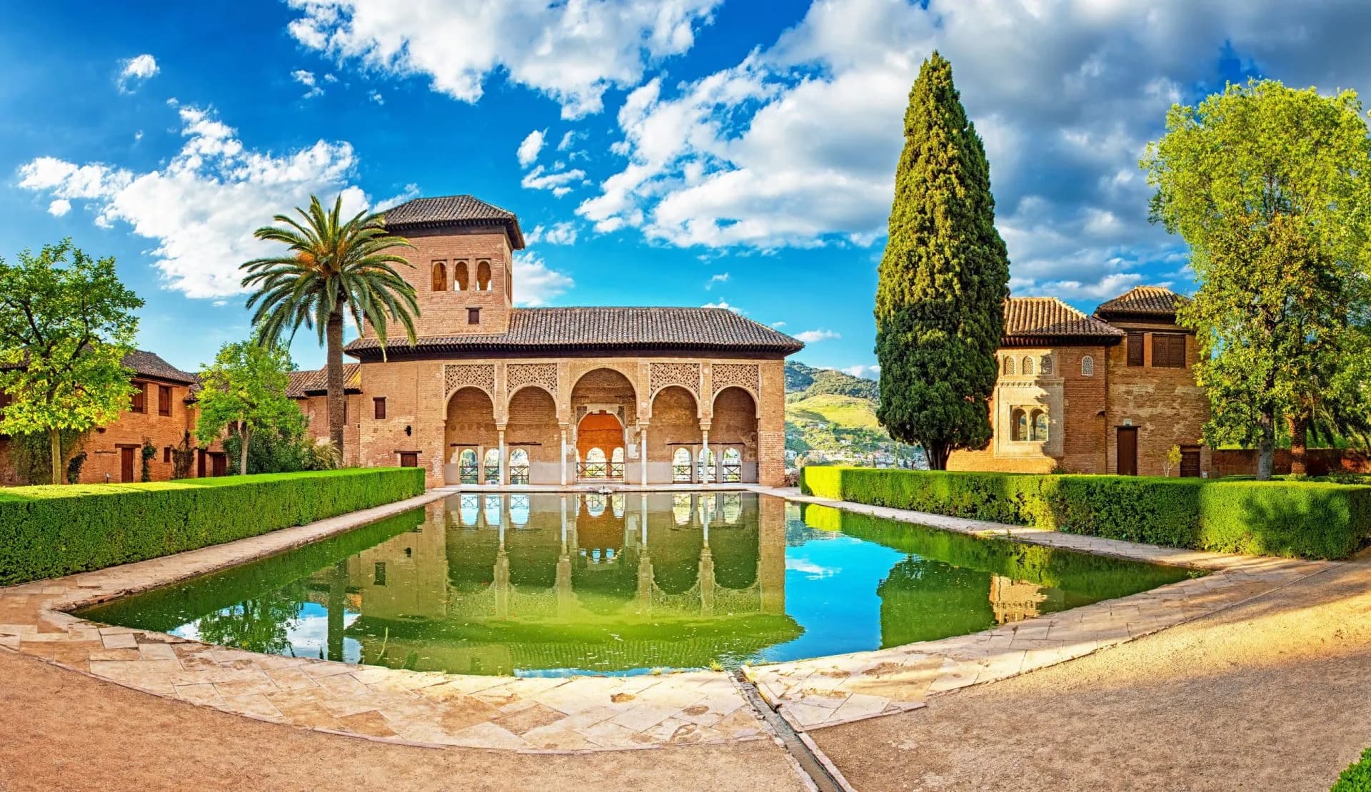Palace in the famous Alhambra in Granada, Spain, with reflection pool and cypress tree.