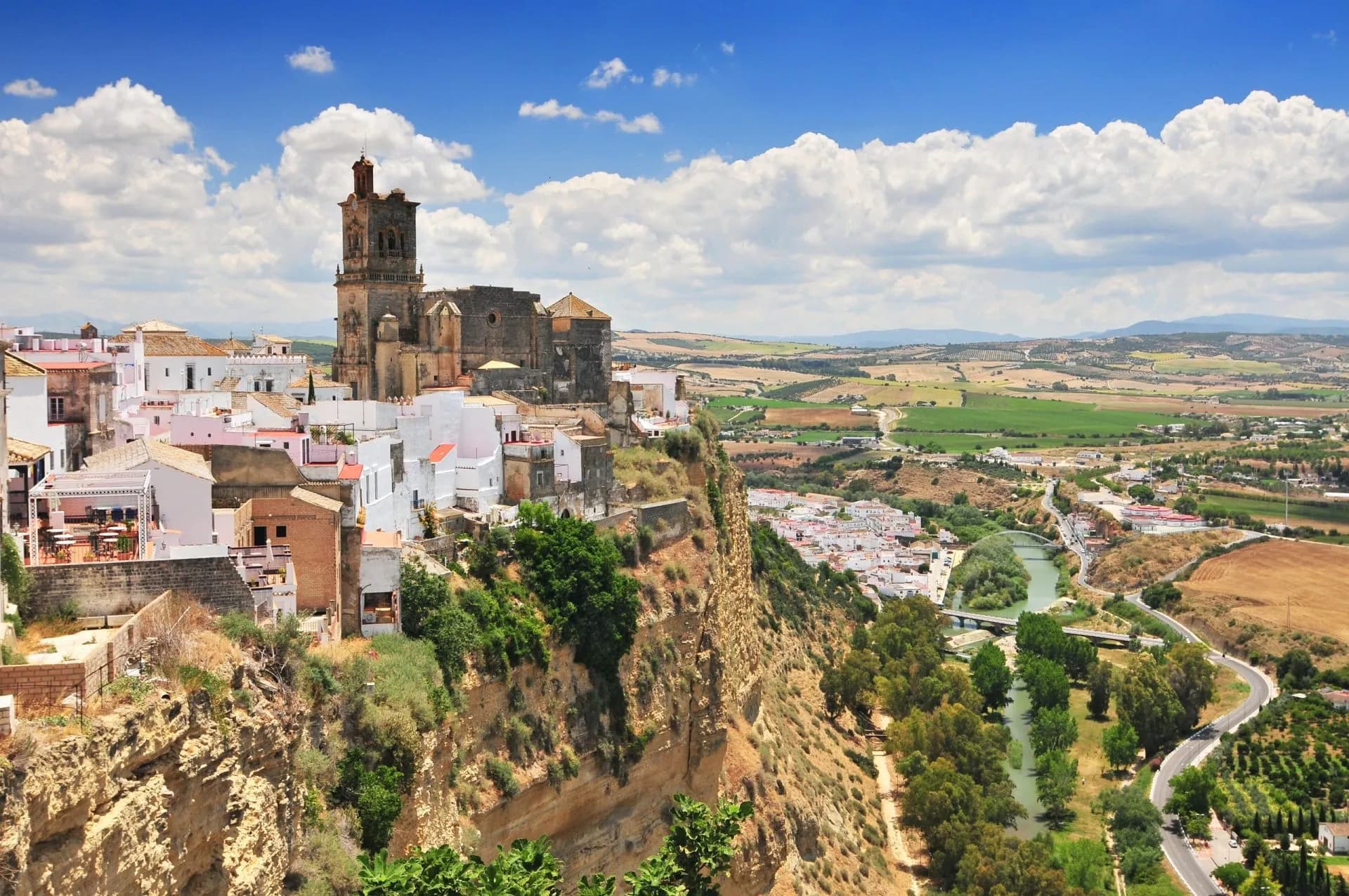 White village perched on a cliff with a historic church overlooking rolling green and brown fields in Arcos de la Frontera...
