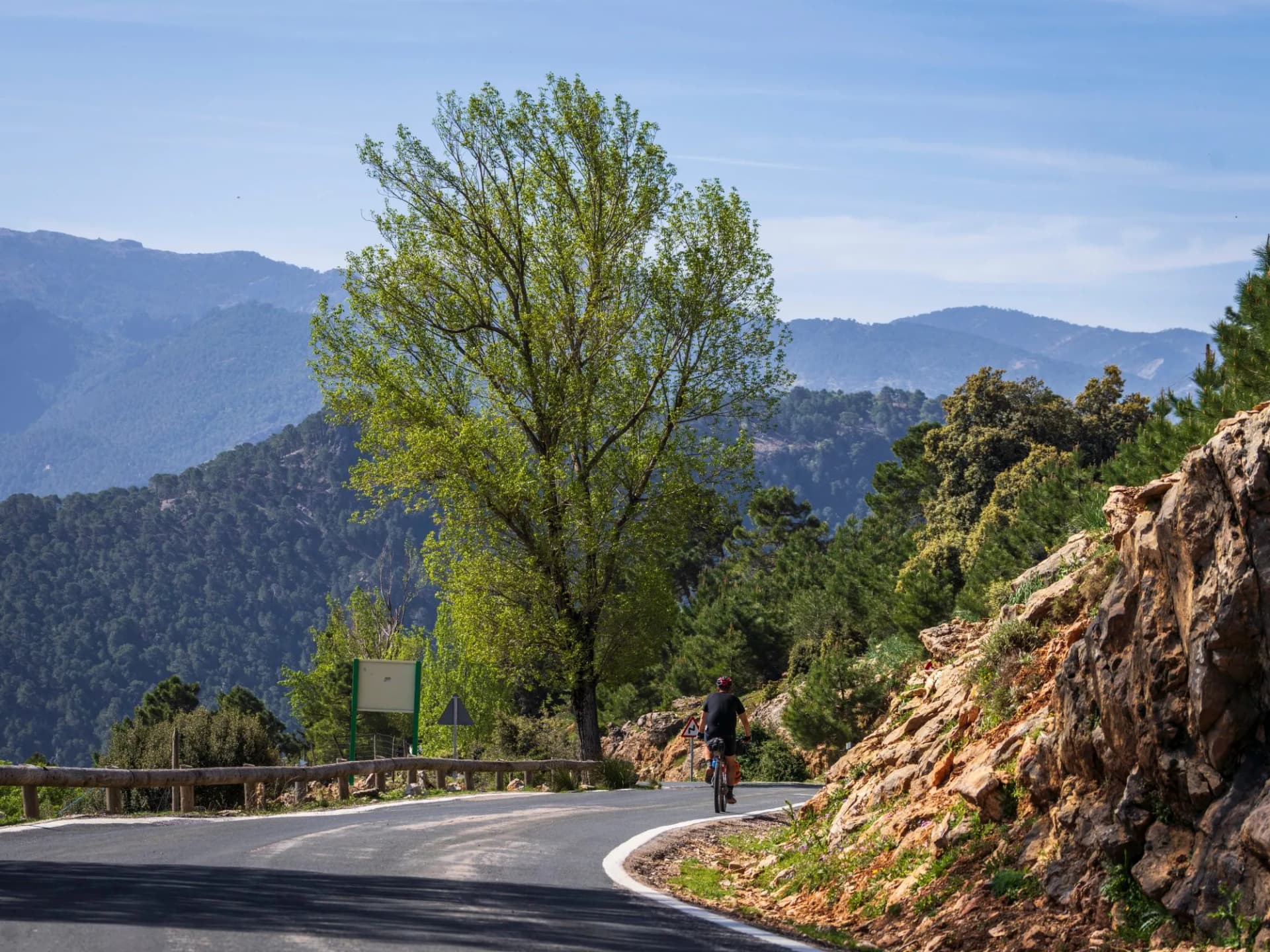 Cyclist riding on winding road through mountains in Sierra de Cazorla Natural Park, Jaén, Spain.