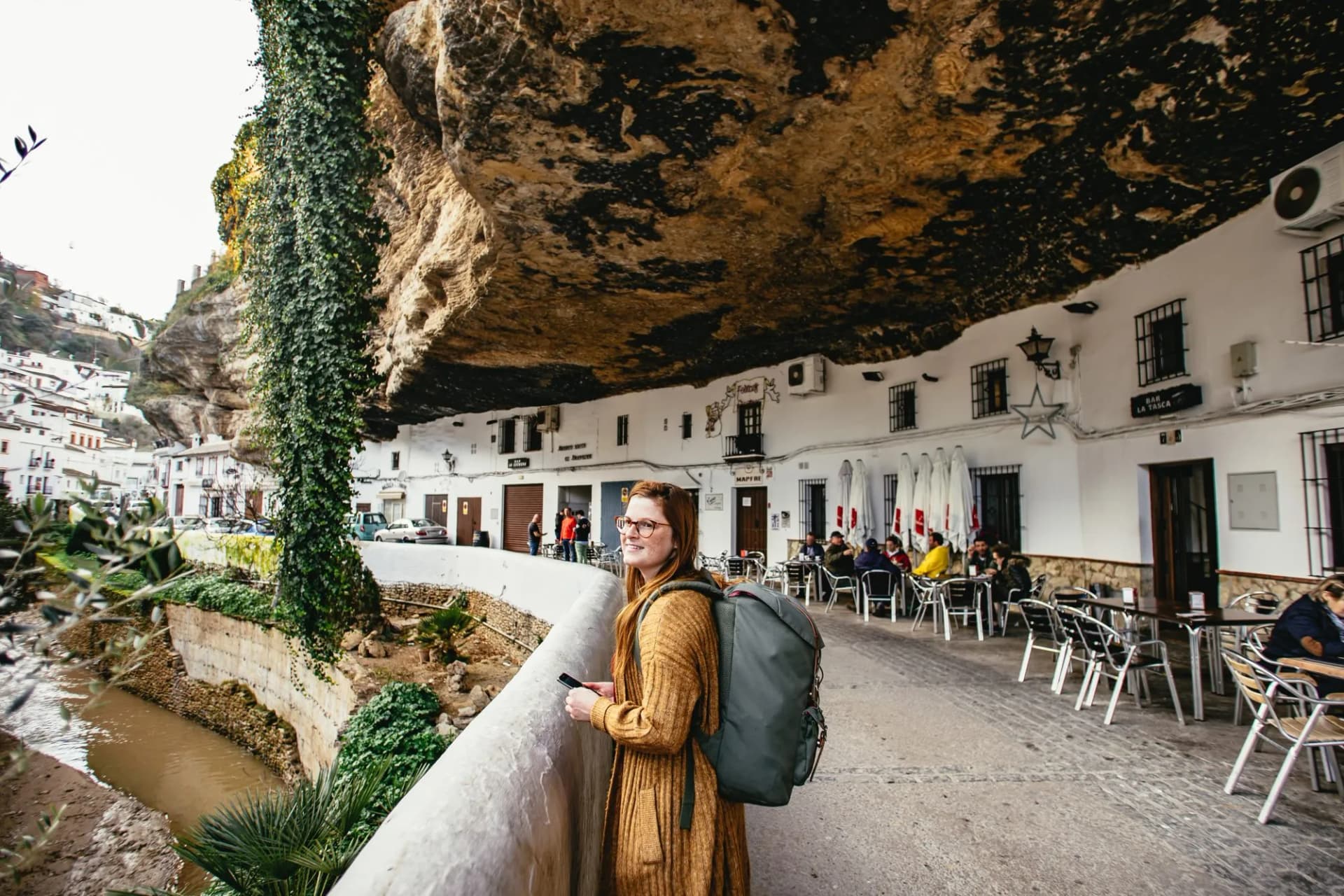 Backpacker admiring town built under massive rock overhang near river in white village