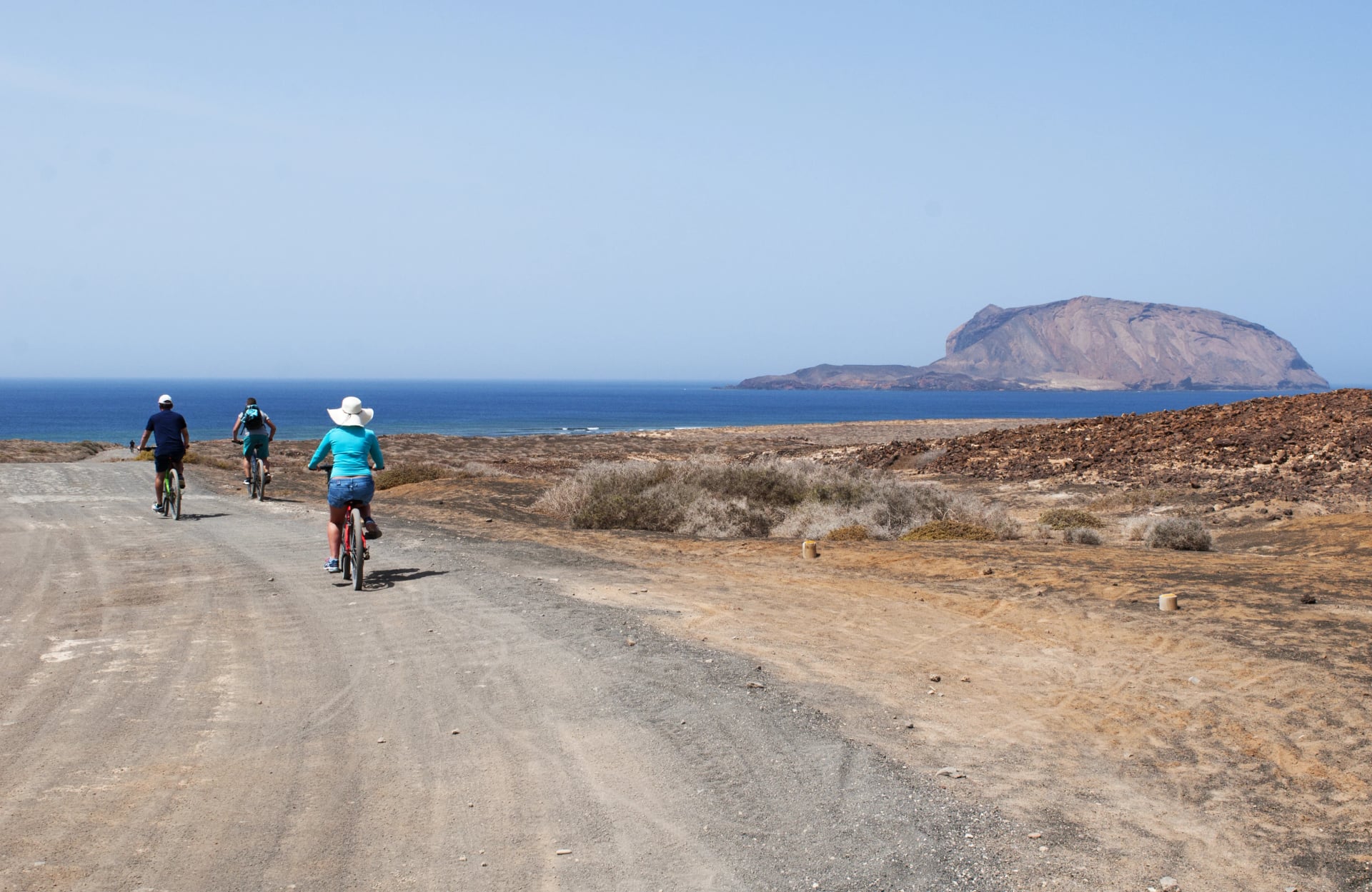 Lanzarote, De Kanariske Øer: turister set bagfra på cykel på den grusede vej til stranden Playa de Las Concisa på øen La Graciosa