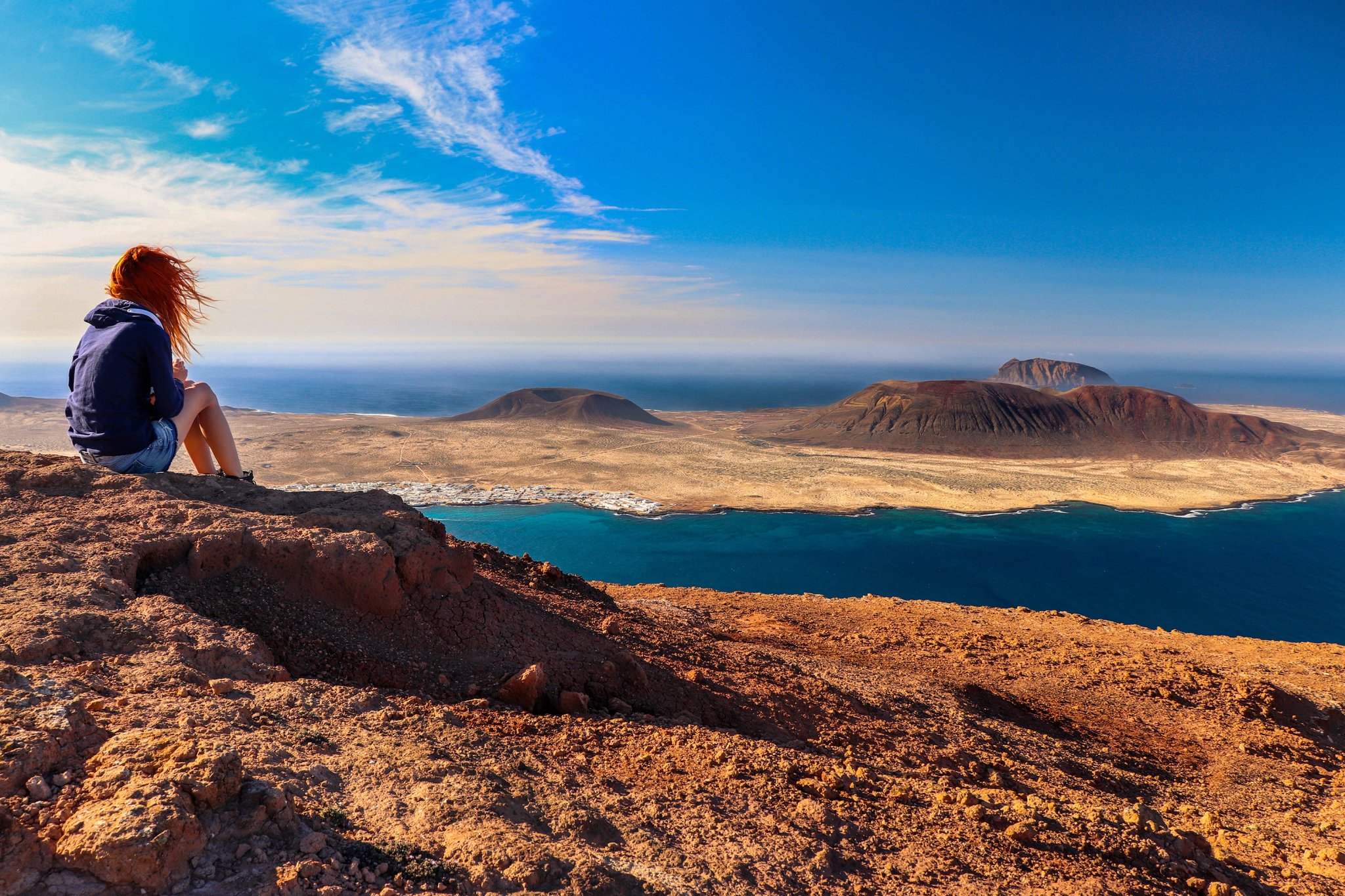 A woman looking at the sea and the island. Location: Europe, Spain, Canary Islands, Lanzarote (near Mirador del Rio; La Graciosa island in the background)