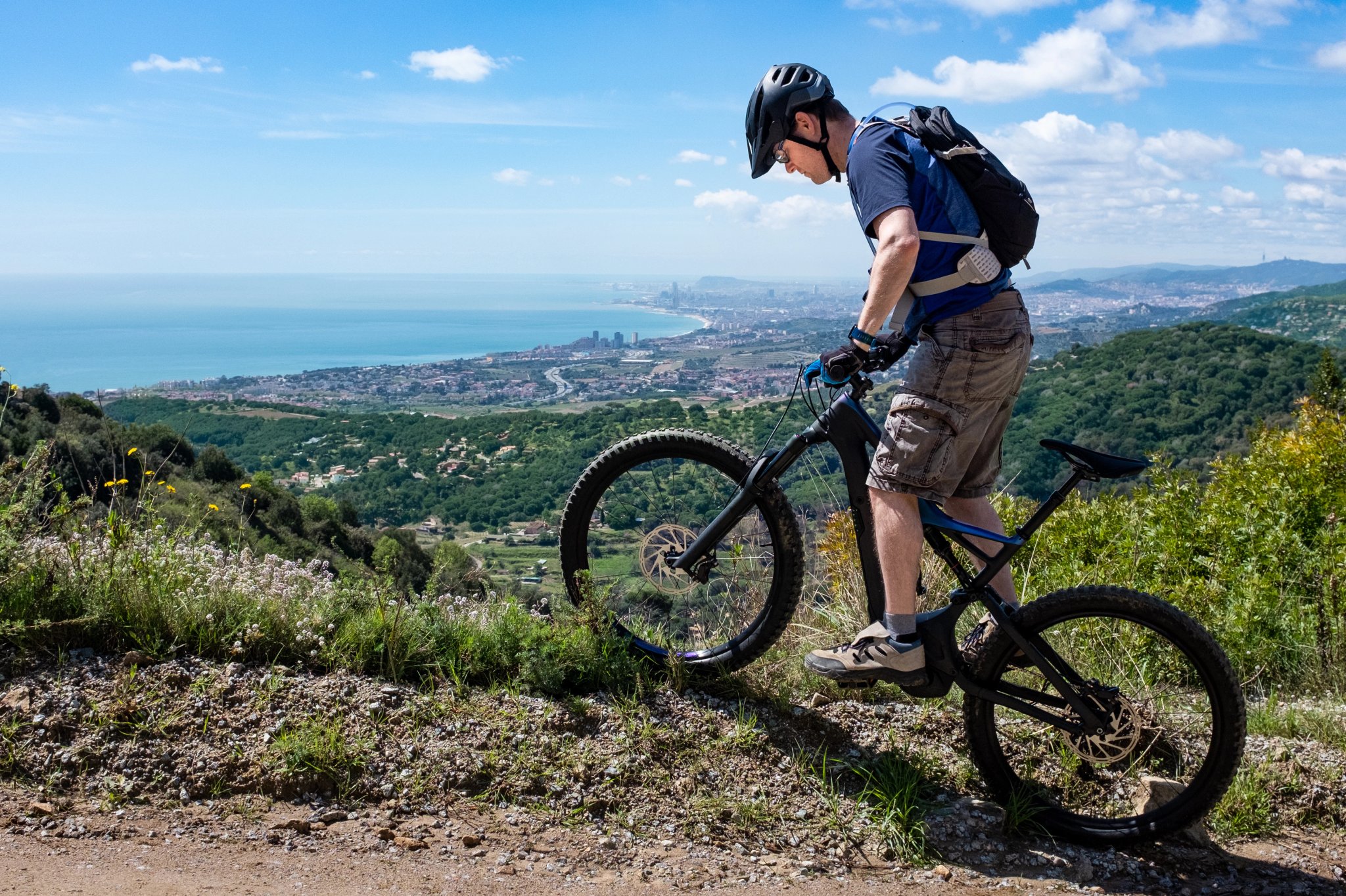 Ung manlig mountainbikecyklist på en elcykel som balanserar på gränsen till en bergsväg, Barcelona Spanien i bakgrunden