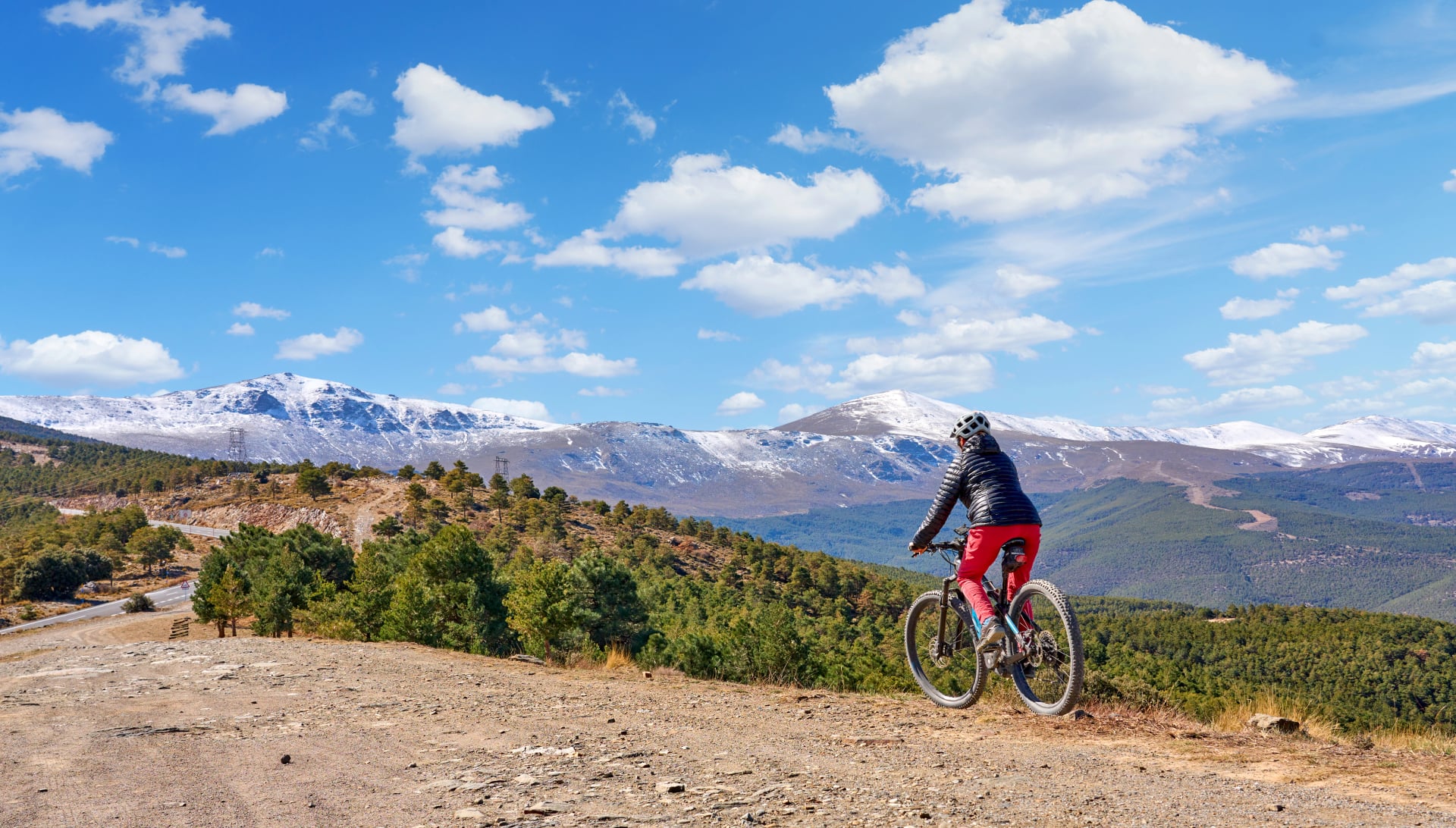 fin, aktiv senior kvinne som sykler med sin elektriske terrengsykkel under de snødekte fjellene i den spanske Sierra Nevada, nær Granada, Andalusia, Spania