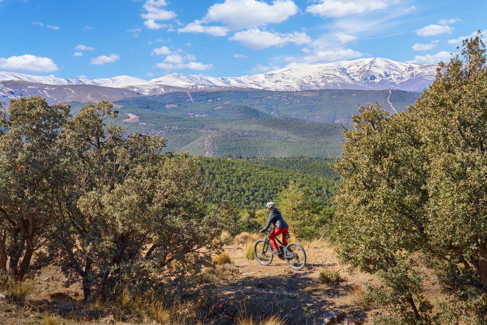 fin, aktiv senior kvinne som sykler med sin elektriske terrengsykkel under de snødekte fjellene i den spanske Sierra Nevada, nær Granada, Andalusia, Spania
