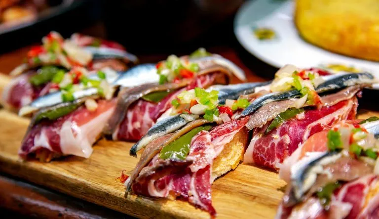 Appetittvekkende spanske tapas med jamon, ansjos og grønne grønnsaker på trebrett i nærbilde i San Sebastian, Donostia, Spania.