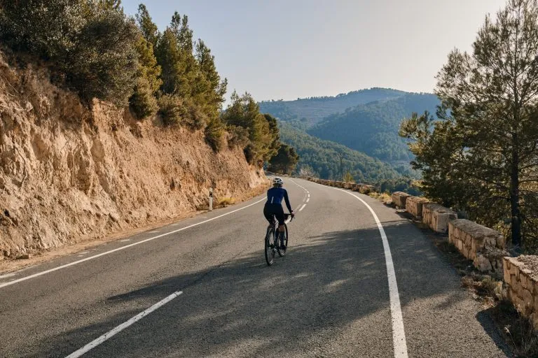 Giovane ciclista in forma che pedala sulla strada su una bicicletta di ghiaia al tramonto.Silhouette di una ciclista donna sullo sfondo delle montagne.Regione di Alicante in Spagna