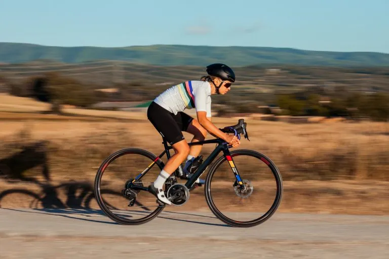 Giovane atleta professionista bionda che scende dalla collina molto velocemente con la sua tuta da ciclismo bianca e sulla sua bicicletta nera.